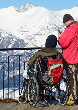 Zwei Personen auf Aussichtsterasse im Winter. Eine Person im Rollstuhl, daneben eine Person stehend.